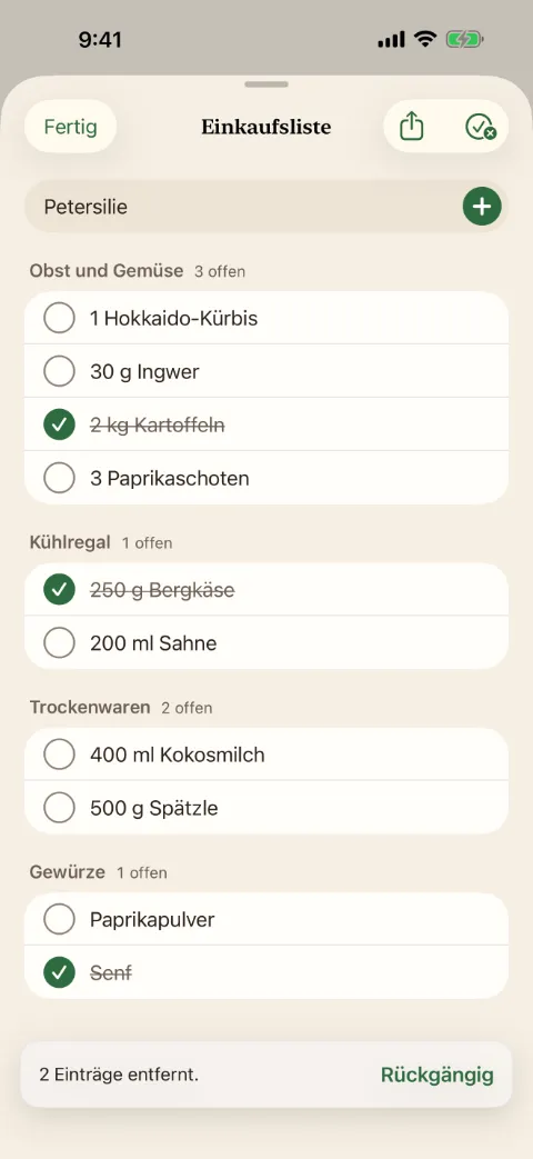 Die Einkaufsliste in Kochzettel mit den Gängen Obst und Gemüse, Kühlregal, Trockenwaren und Gewürze. Drei Einträge sind abgehakt und durchgestrichen.