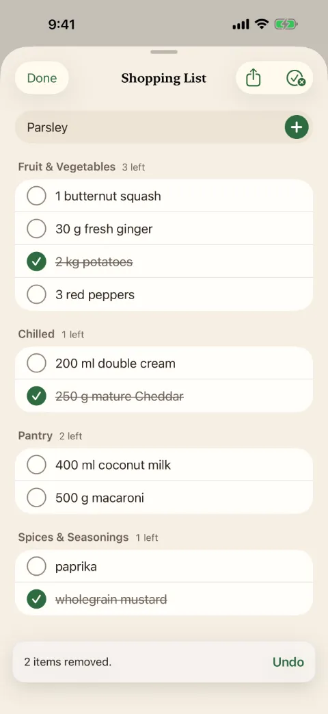 Capture de Kochzettel en anglais. La liste de courses avec les rayons fruits et légumes, frais, épicerie, épices et condiments. Trois articles sont cochés et barrés.